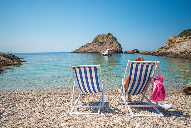 Rear view of woman sitting on deck chair at beach. Female tourist is at idyllic Vis Island during vacation. She is relaxing on shore at island during summer.